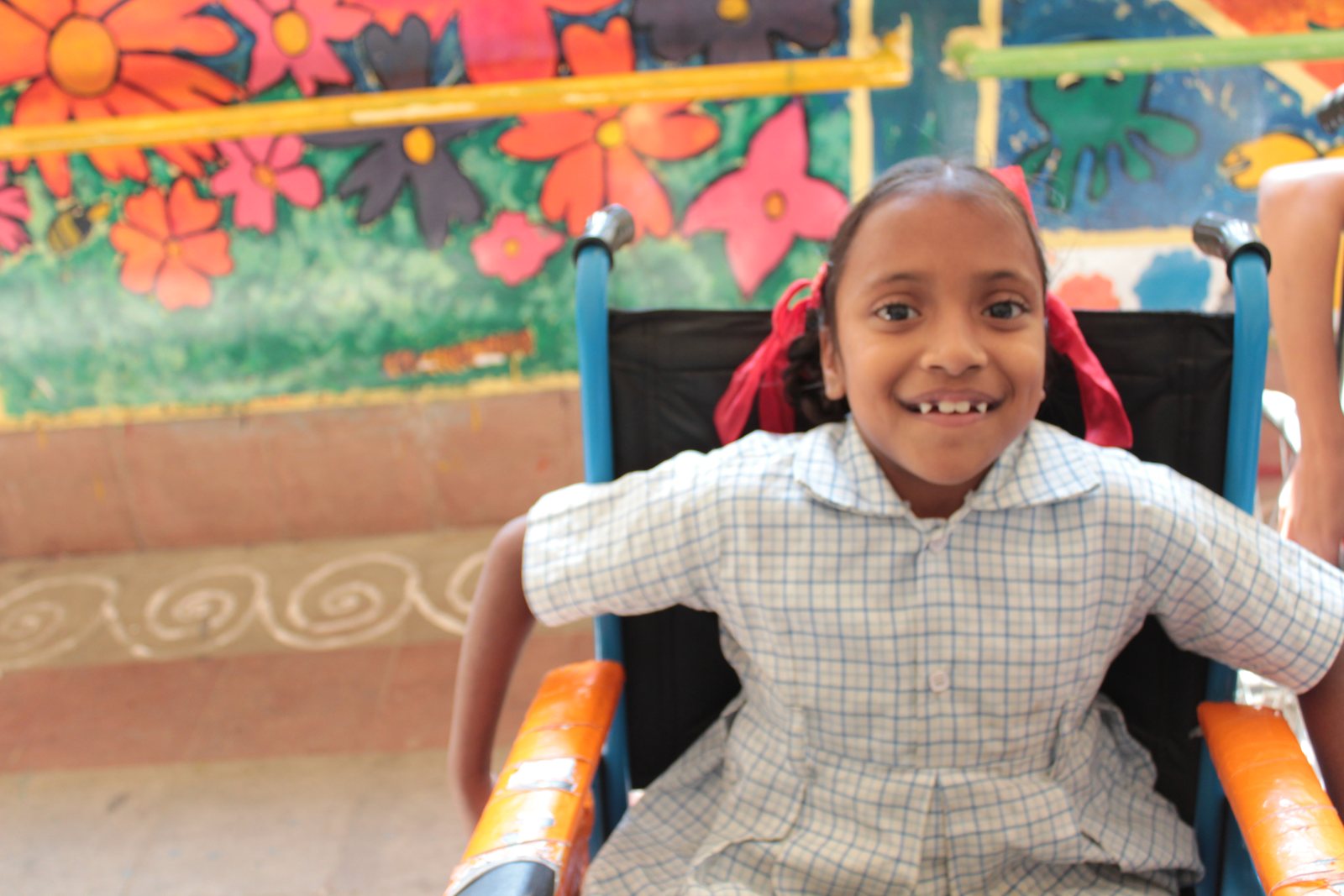 A student smiling in her wheelchair in front of a brightly painted garden mural at school
