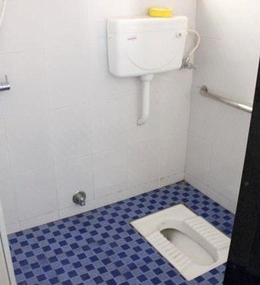 The rebuilt bathroom: a clean accessible squat toilet with a wall-mounted grab bar and tiled floor