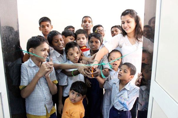 Students holding scissors and cutting a green ribbon across the doorway of the new bathrooms