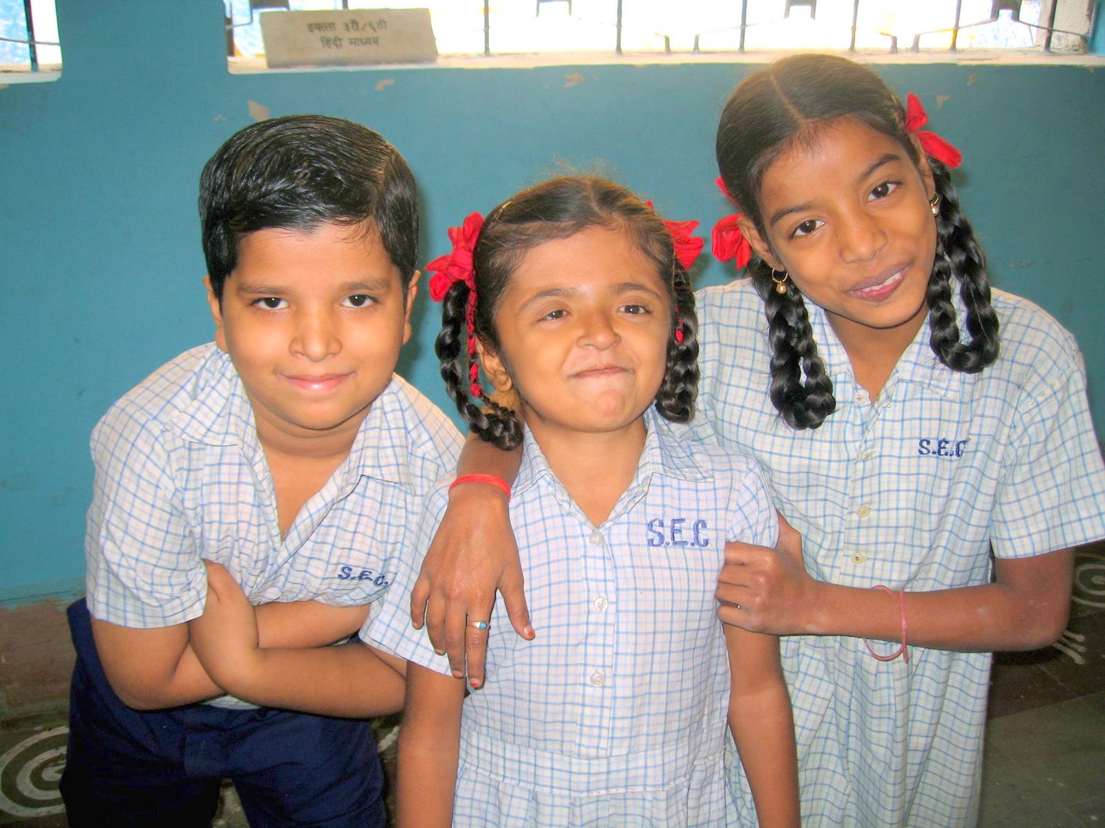 Three students standing arm in arm outside their classroom, smiling