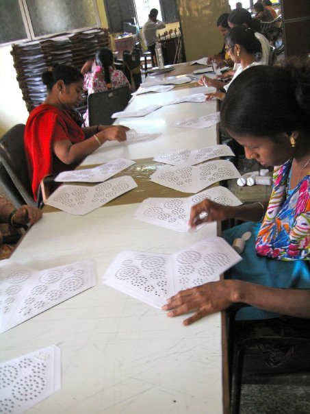 Students seated along a long table doing detailed paper and craft work